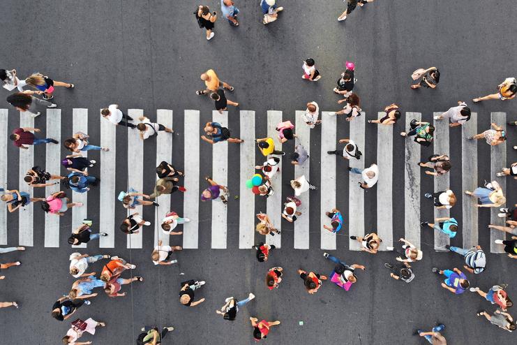 Luftaufnahme von Menschen auf einem Zebrastreifen Viele Menschen überqueren einen breiten Zebrastreifen aus der Vogelperspektive. Die Personen tragen bunte Kleidung und sind in Bewegung auf einer belebten Straße.