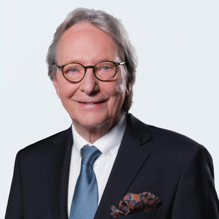 Porträt von Dr. Jürgen Apel Dr. Jürgen Apel, ein älterer Herr mit Brille und grauen Haaren, trägt einen dunklen Anzug, blauen Schlips und ein farbiges Einstecktuch, während er freundlich in die Kamera lächelt.