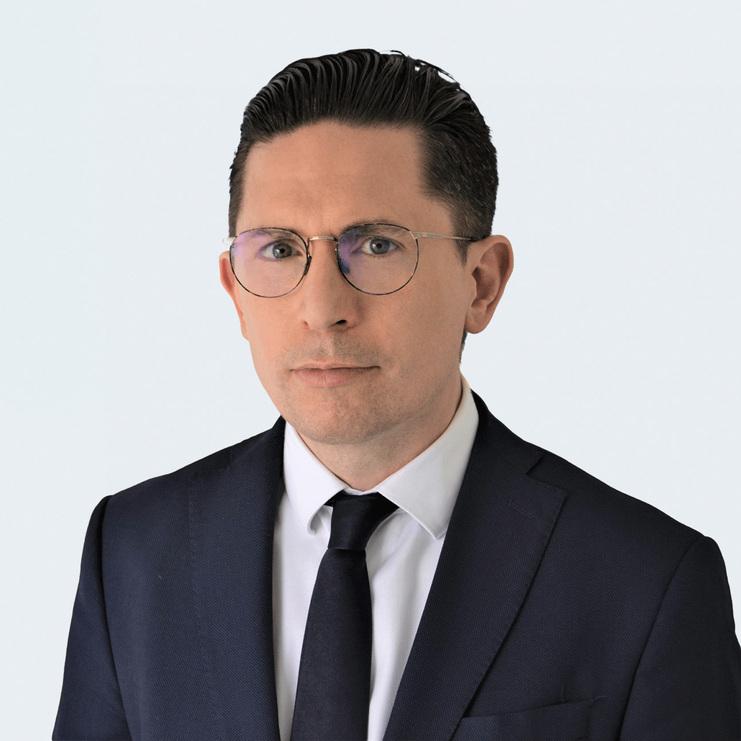 Porträt von Daniel Pohl, LL.M. Daniel Pohl, LL.M., ein Mann mit Brille und zurückgekämmtem Haar, trägt einen dunkelblauen Anzug, ein weißes Hemd und eine dunkle Krawatte. Er blickt ernst in die Kamera vor hellem Hintergrund.