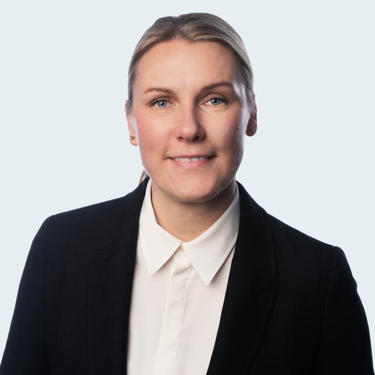 Porträt von Katja Goldbach, LL.M. Katja Goldbach, LL.M., eine Frau mit blondem Haar, trägt einen schwarzen Blazer über einer weißen Bluse. Sie lächelt freundlich und blickt direkt in die Kamera vor einem hellen Hintergrund.